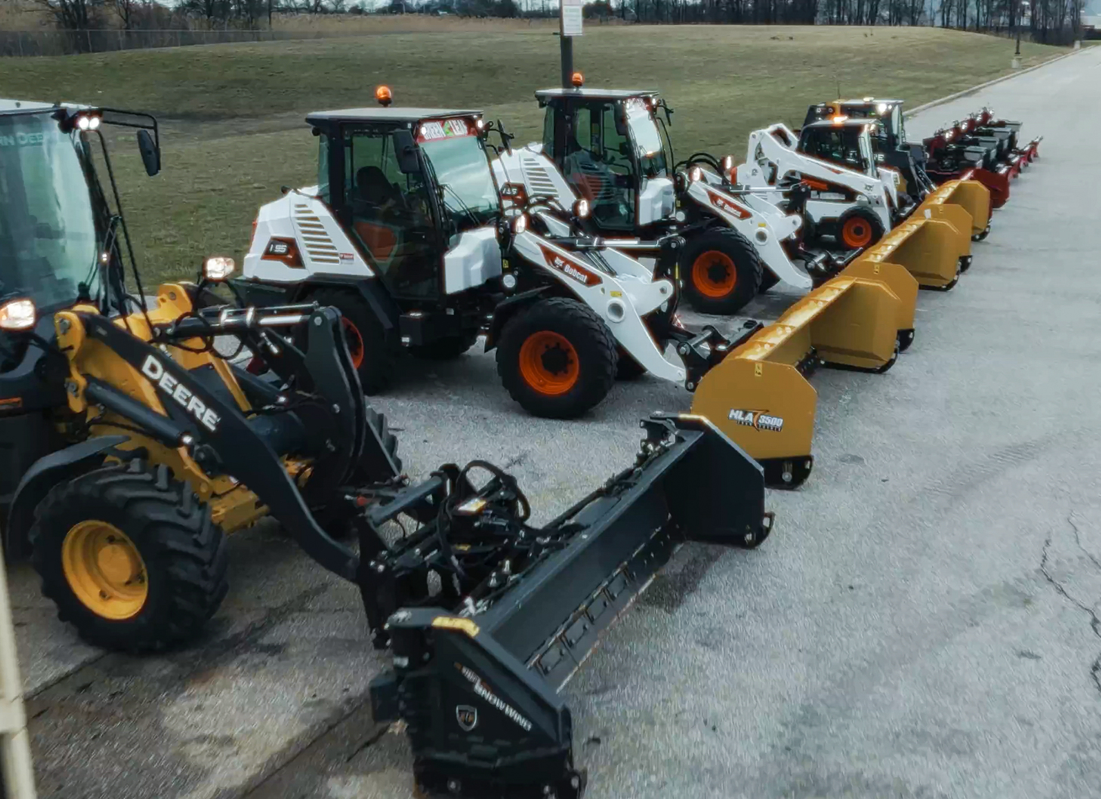 Professional winter maintenance equipment lineup with John Deere tractors and snow removal attachments